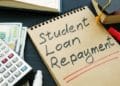 Student loan repayment sign, notepads, calculator and cash.