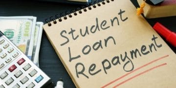 Student loan repayment sign, notepads, calculator and cash.