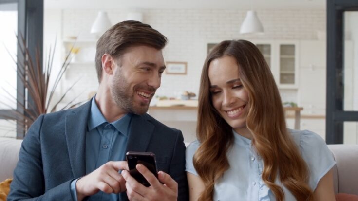 A couple sitting together and smiling while looking at a smartphone