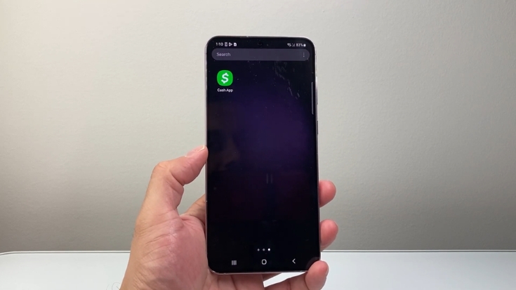 Hand holding a smartphone with the Cash App icon visible on the screen