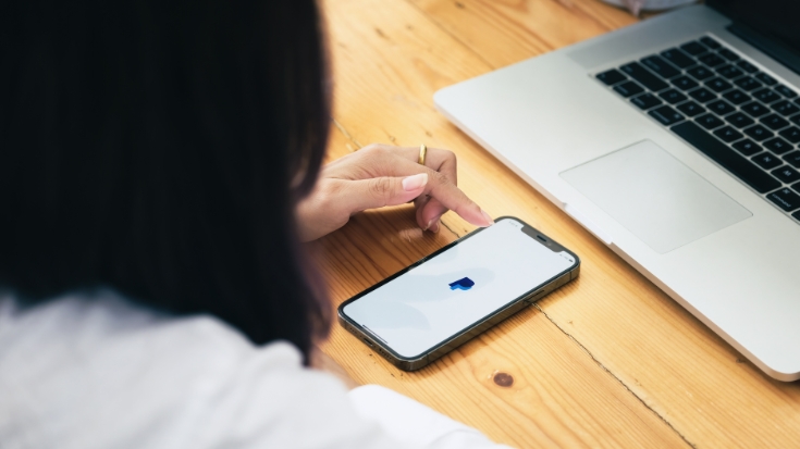 Person using the PayPal app on a smartphone next to a laptop