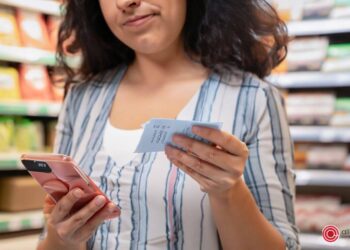 a woman with a supermarket receipt in one hand and her cellphone in the other