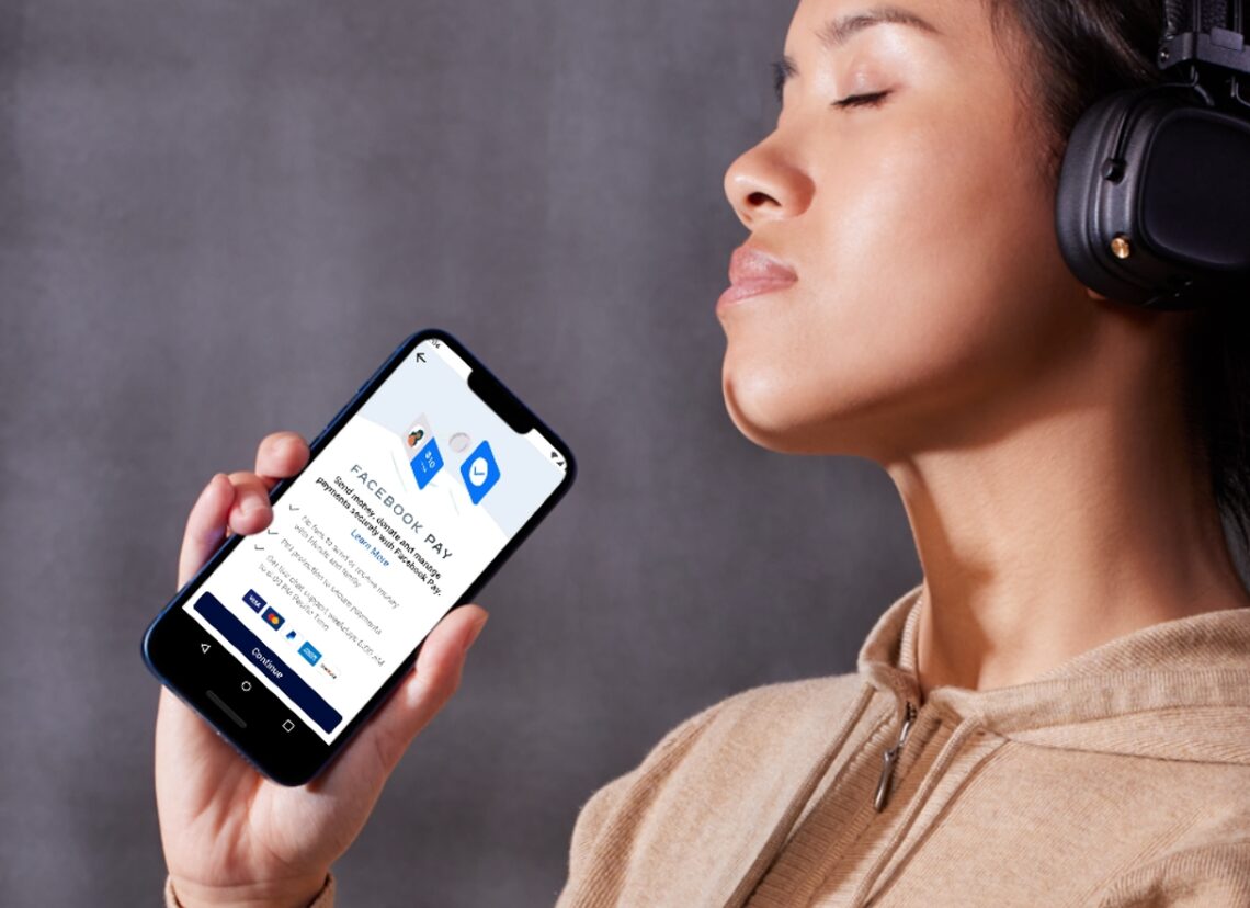 A woman holding a phone displaying the Facebook Pay app with headphones on her head, symbolizing the concept of earning through views on Facebook.
