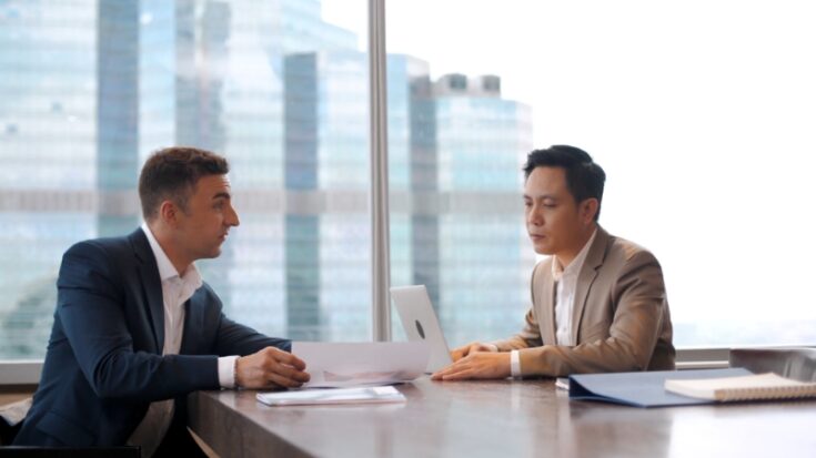 Two colleagues discuss work at a desk as employers assess communication and soft skills in a real setting