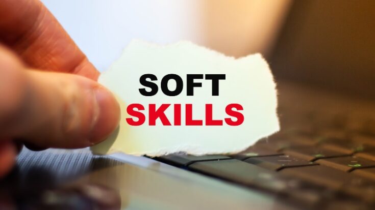 Hand holding paper with “soft skills” text above a laptop keyboard