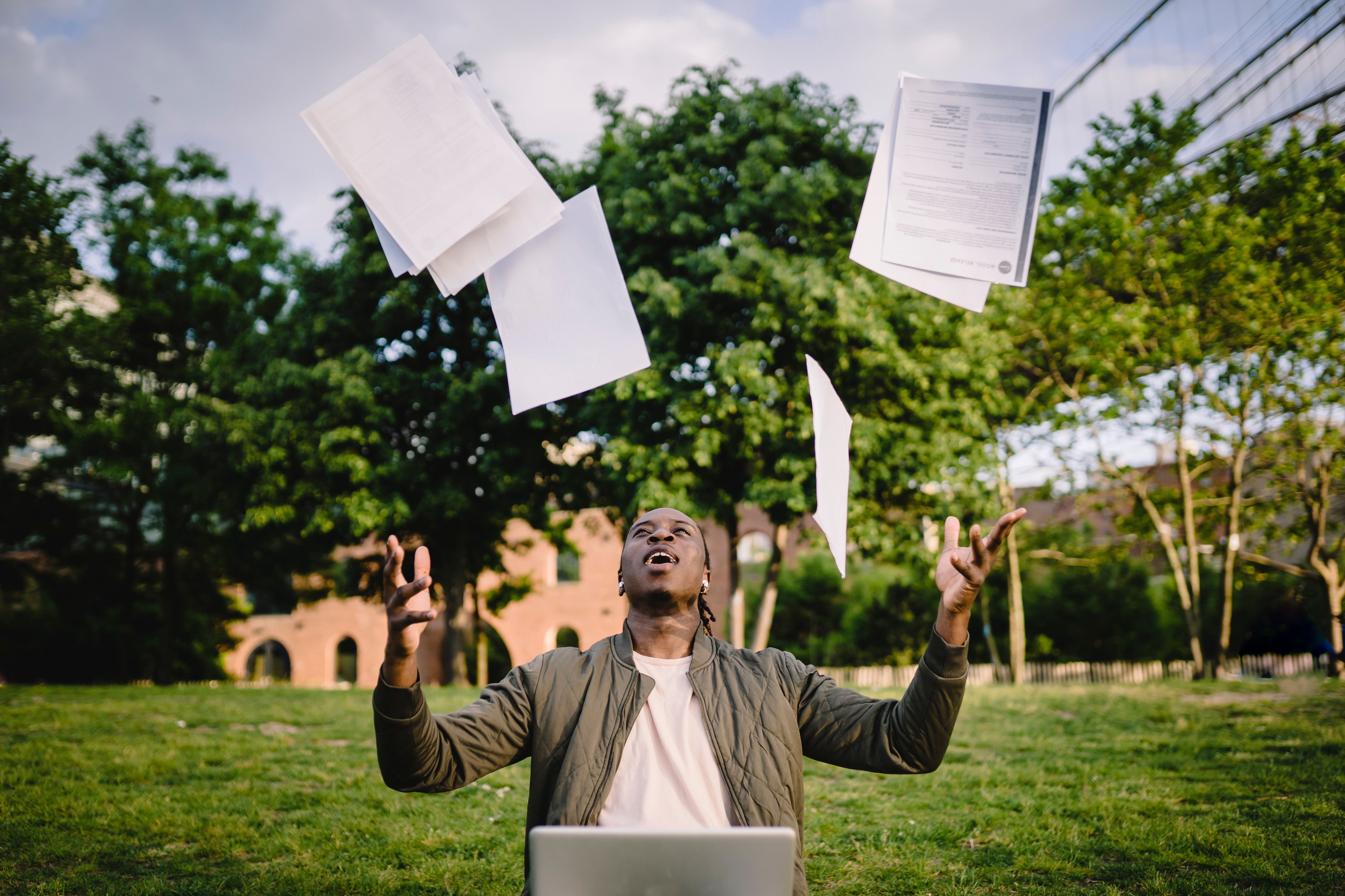 Graduate celebrating a successful job search with resumes and a laptop outdoors